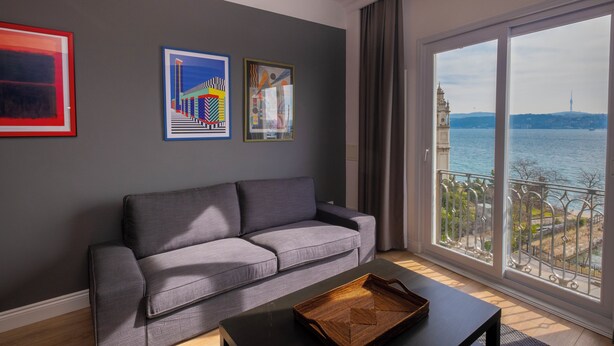 A modern living room with a grey sofa, a black coffee table, and a large window with a view of a cityscape and a body of water. - Hip 2BR Apartment · Bosphorus & Dolmabahçe View · Central Beyoğlu (Beyoğlu, İstanbul)