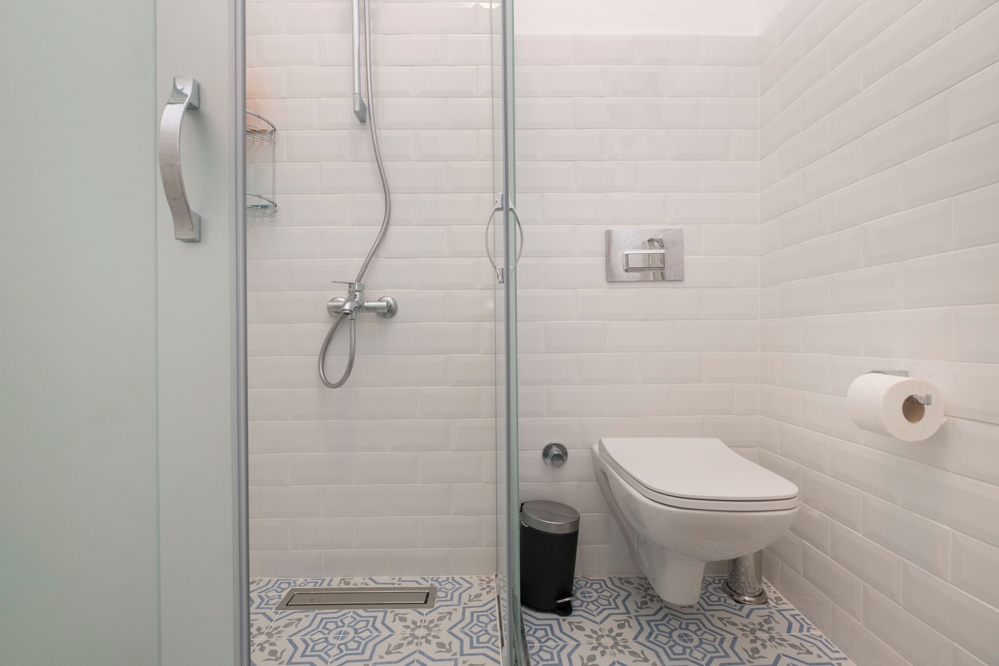 A modern bathroom with a glass-enclosed shower, a toilet, and a trash bin.