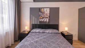 A modern hotel room with a large bed, two bedside tables with lamps, a wall-mounted air conditioner, and a cityscape painting above the bed. - Hip 2BR Apartment · Bosphorus & Dolmabahçe View · Central Beyoğlu (Beyoğlu, İstanbul)