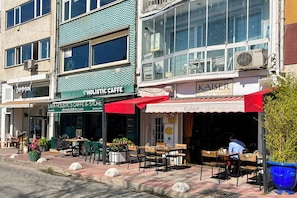 A street view with outdoor seating at a cafe and a building with a sign reading 'KAISER'.