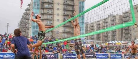 A beach volleyball game with spectators and a Bud Light advertisement in the background.
