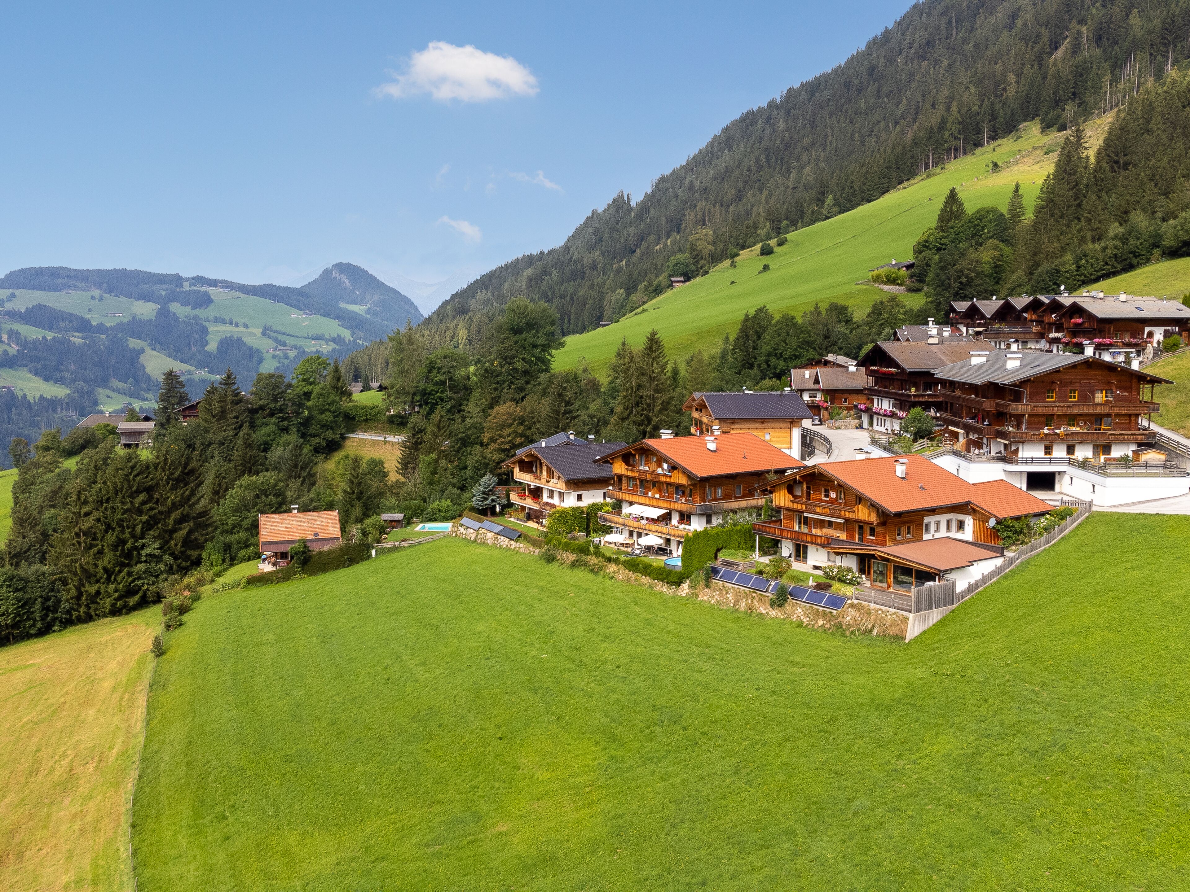 Un chalet situé sur une colline, composé de plusieurs bâtiments en bois, doté d’une piscine et de panneaux solaires.