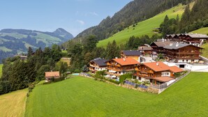 A hillside chalet with multiple wooden buildings, a swimming pool, and solar panels.