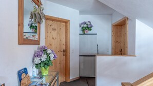 A hallway with wooden doors, a mirror, a vase with flowers, and a small table with brochures and a plant.
