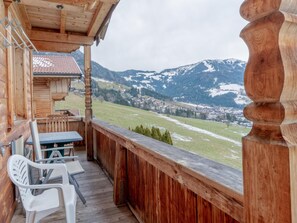 Un balcon en bois avec une table et des chaises, donnant sur un paysage montagneux enneigé.