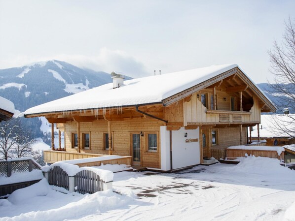 Un chalet en bois doté d’un balcon, entouré de montagnes enneigées.
