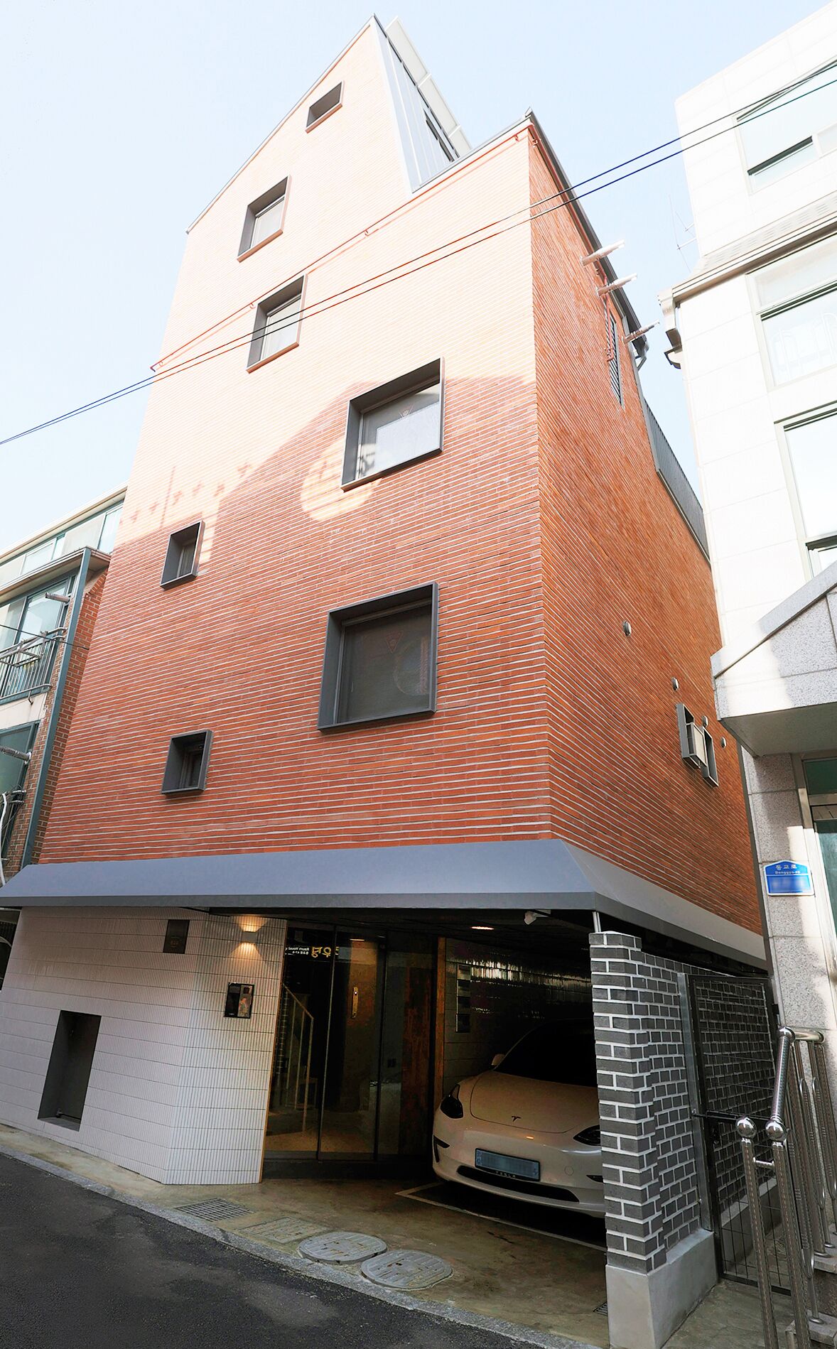 Un immeuble à plusieurs étages, doté d’une façade en briques, d’une entrée couverte et d’une voiture garée dans l’allée.
