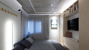 Ein modernes Hotelzimmer mit Bett, Fernseher, einem kleinen Tisch mit Obstschale und einer Bücherregal.