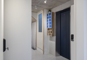 Un pasillo con una puerta, un ventanal con marco azul y un estante con objetos.