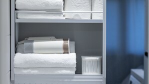 Ein weißer Stauraum mit Regalen, auf denen ordentlich gefaltete weiße Handtücher und ein weißer Fön liegen.