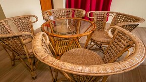 Una mesa redonda de mimbre con seis sillas, una superficie de vidrio y una cortina roja al fondo.