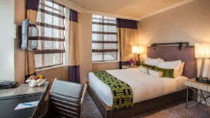 Una habitación de hotel con una cama, mesitas de noche, un escritorio y una silla.