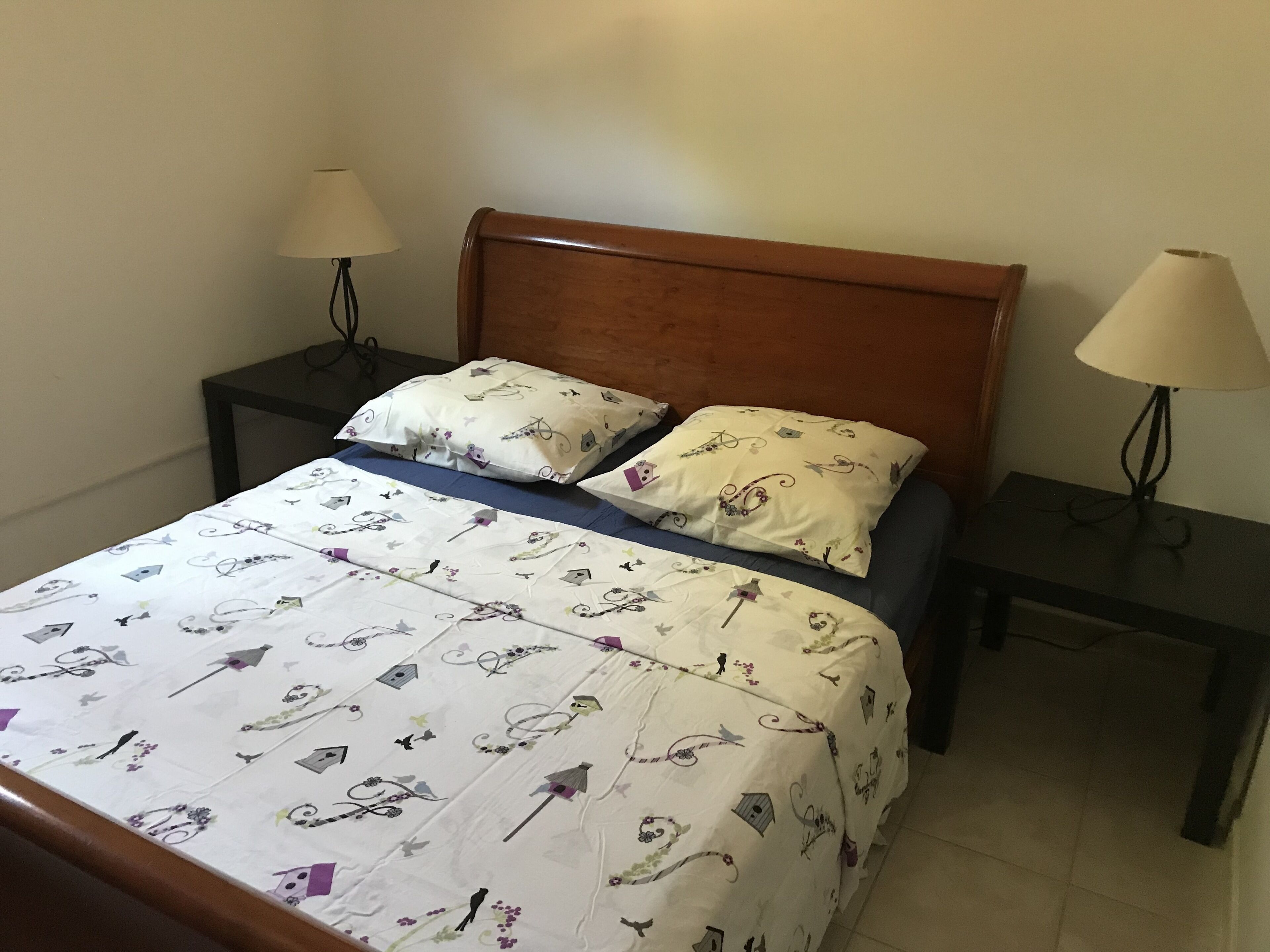 Een bed met een bloemenprintdeken, twee kussens en twee nachtkastjes met lampen.