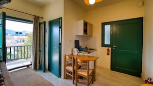 A compact kitchen with a dining table and chairs, a green door, and a view of the outdoors. - erodios apartments (Apokoronas)