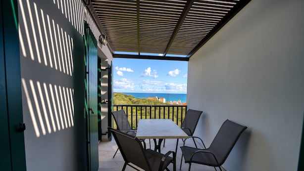 A balcony with a table and chairs, overlooking a scenic view of the sea and hills. - erodios apartments (Apokoronas)