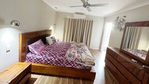 A bedroom with a wooden bed, a ceiling fan, a mirror, and a window with curtains. - Beautiful modern family home ,centrally located ,close to everything (Bli Bli)