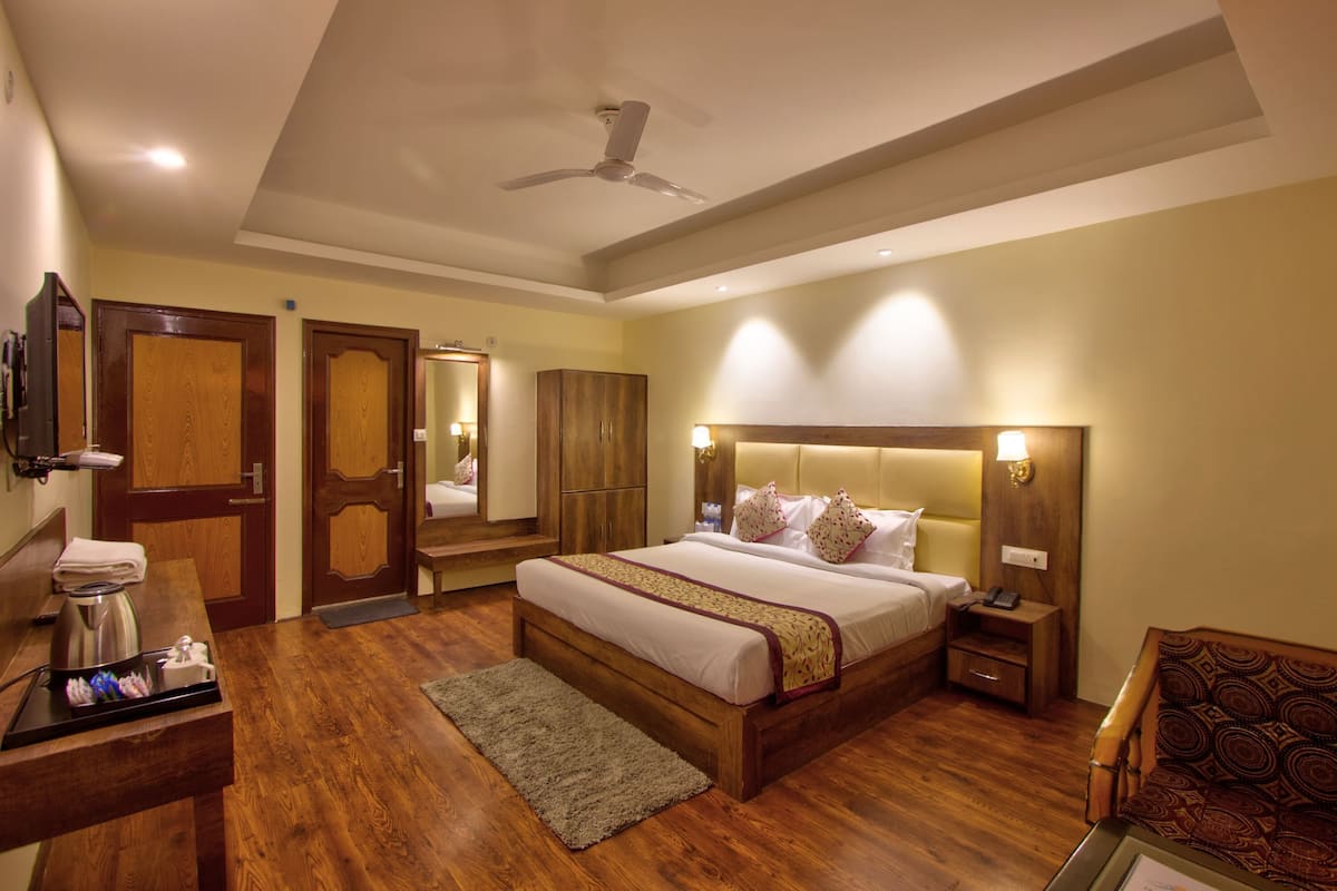 A hotel room with a bed, bedside table, nightstand, and a wooden floor.
