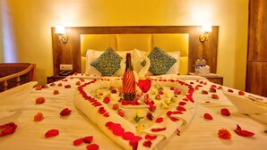 A neatly made bed with a heart-shaped arrangement of rose petals and a bottle of champagne. - Sunrise Villa Manali (Manali)