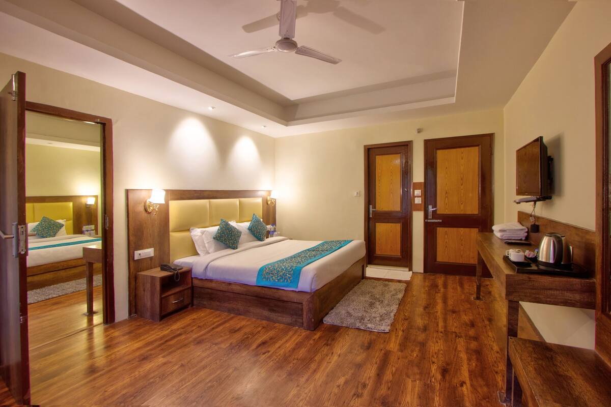A hotel room with a wooden bed, bedside tables, a desk with a chair, a mirror, and a ceiling fan.
