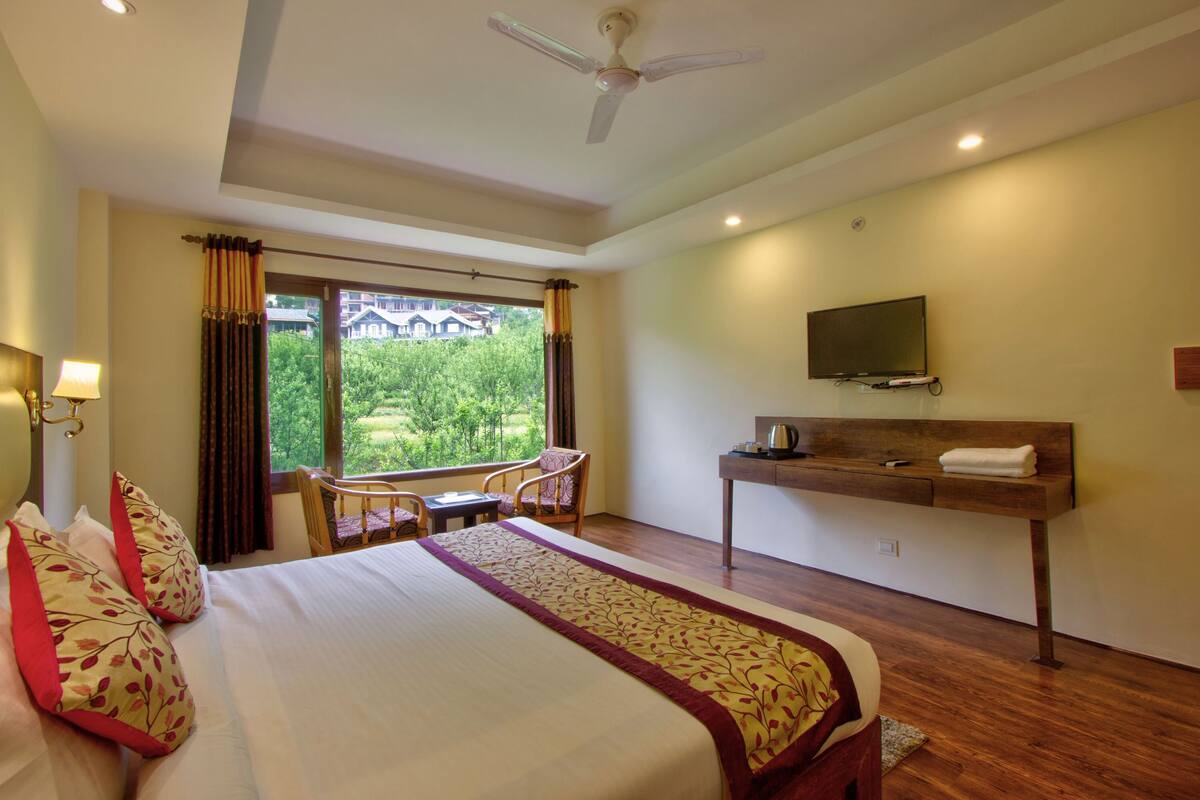 A hotel room with a bed, a desk, a chair, a television, and a window with curtains.