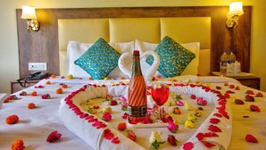 A hotel room with a neatly made bed, a bottle of champagne, and a glass of red wine on the bed. - Sunrise Villa Manali (Manali)