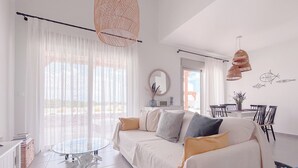A modern living room with a sofa, a glass coffee table, and wicker pendant lights. - Stylish Beach House 4 BR w/pool - 1 min from the beach! (Rhodes)