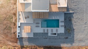 An aerial view of a modern house with a swimming pool, outdoor seating, and a covered patio area. - Stylish Beach House 4 BR w/pool - 1 min from the beach! (Rhodes)