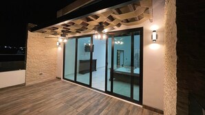 Une terrasse extérieure moderne avec une plateforme en bois, des portes coulissantes en verre donnant sur une chambre et un éclairage d’ambiance.