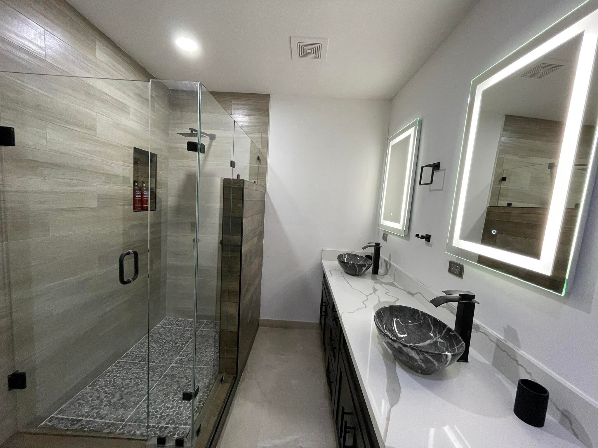 Une salle de bain moderne dotée d’une douche à parois de verre, d’un lavabo en marbre et d’un grand miroir avec éclairage intégré.