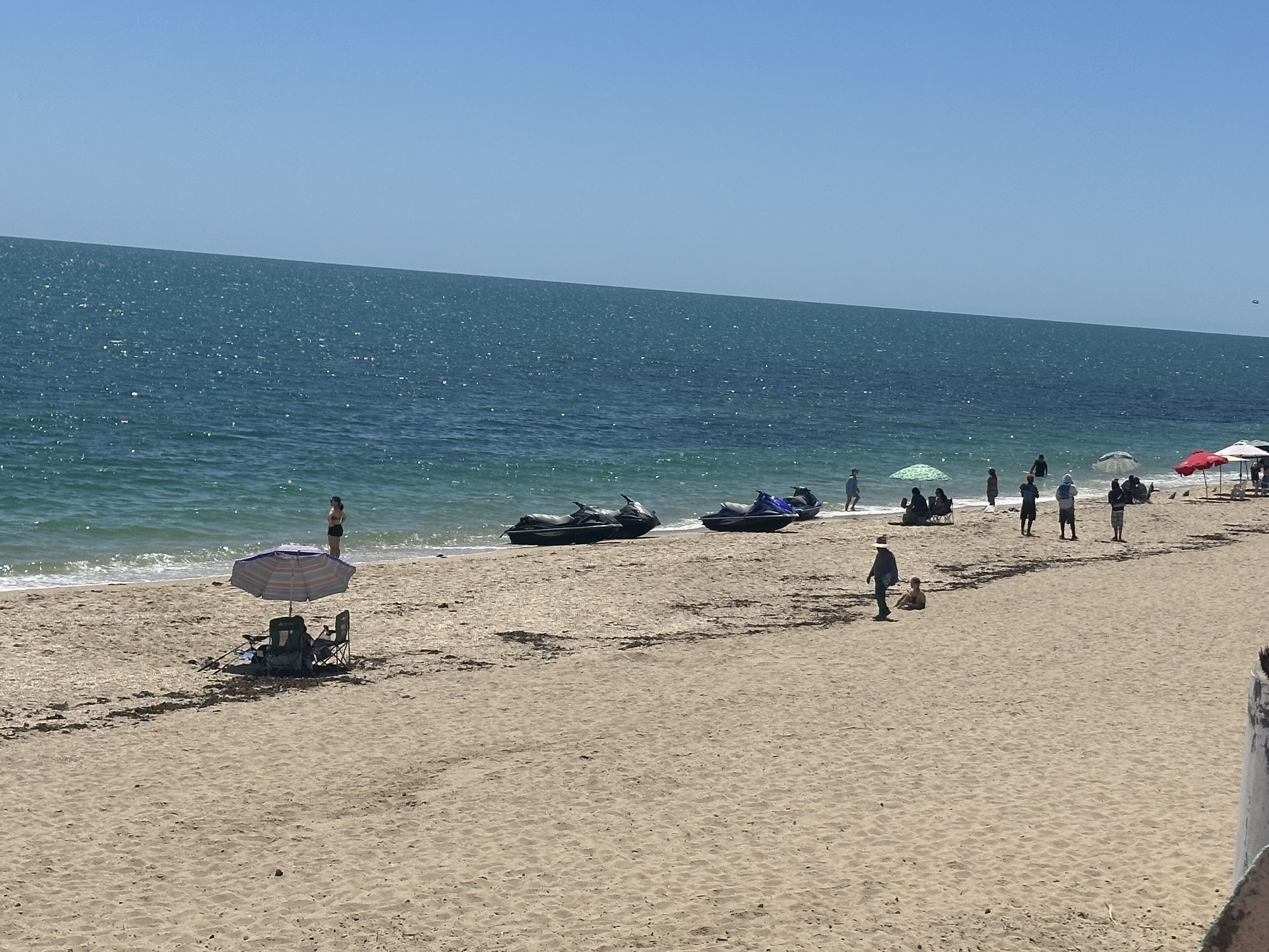 Une plage offrant une vue dégagée sur l’océan, avec plusieurs parasols et quelques personnes.