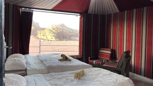 Une chambre avec deux lits, un mur à rayures rouges, une fenêtre donnant sur un paysage désertique et une chaise à rayures rouges et blanches.