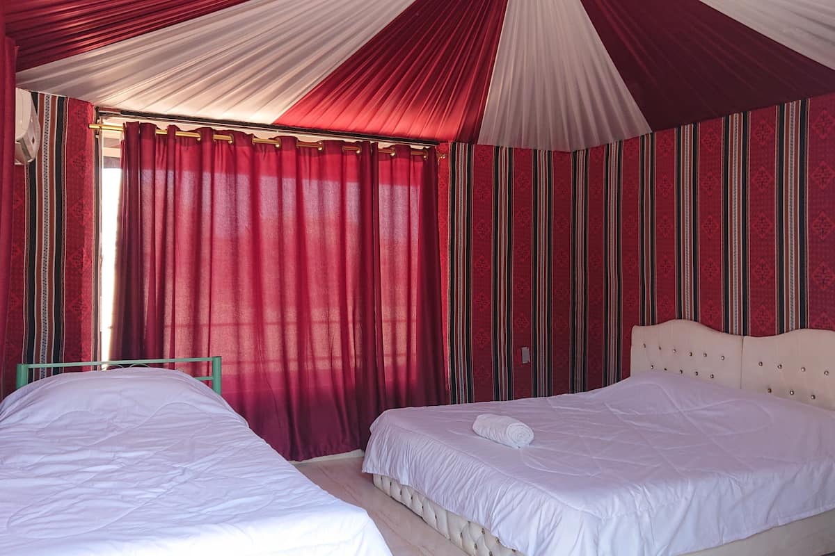 Une chambre avec deux lits, des rideaux rouges et un papier peint à rayures.
