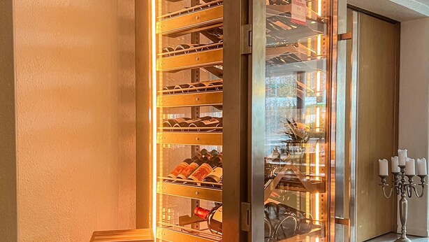 A wine refrigerator with multiple shelves, a wine bottle, and a candle holder. - Apartment Dufour (Rheineck)