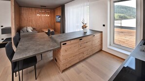 A modern kitchen with a wooden cabinet, a dining table, and chairs. There is a window with a view of a lake and hills.