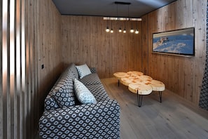 A modern room with a wooden panel wall, a sofa with patterned cushions, a round wooden coffee table, and a mounted TV displaying a snowy landscape. - Tri sestry  (Demanovska Dolina)