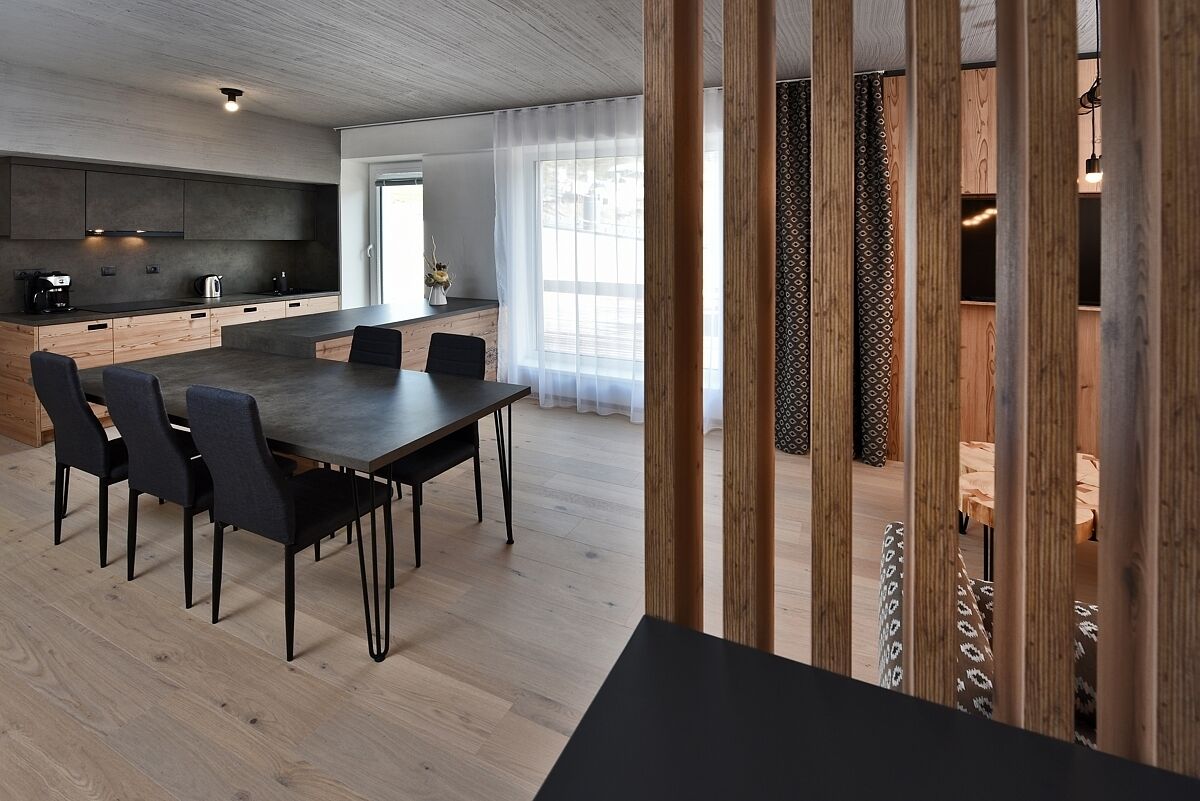 Une cuisine moderne avec des meubles de couleur sombre, un grand îlot central et un coin repas comprenant une table et des chaises de couleur sombre.
