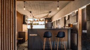 A reception area with a wooden reception desk, two black bar stools, a patterned carpet, and a bar with shelves of bottles.