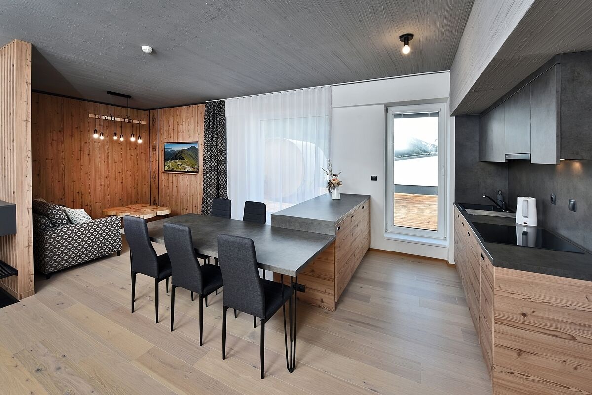 Una cocina moderna con una isla de madera, un comedor con una mesa larga y sillas, y vistas al exterior a través de grandes ventanales.