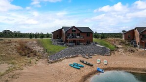 Una casa grande con balcón, una playa arenosa y un pequeño estanque con kayaks.