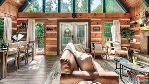 A wooden cabin interior with a high ceiling, a leather sofa, dining area, and a fireplace.