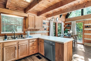 A wooden cabin kitchen with a large island, wooden cabinets, a dishwasher, and a window with blinds.