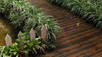 Un sendero de madera con plantas en macetas y un pequeño elemento acuático.