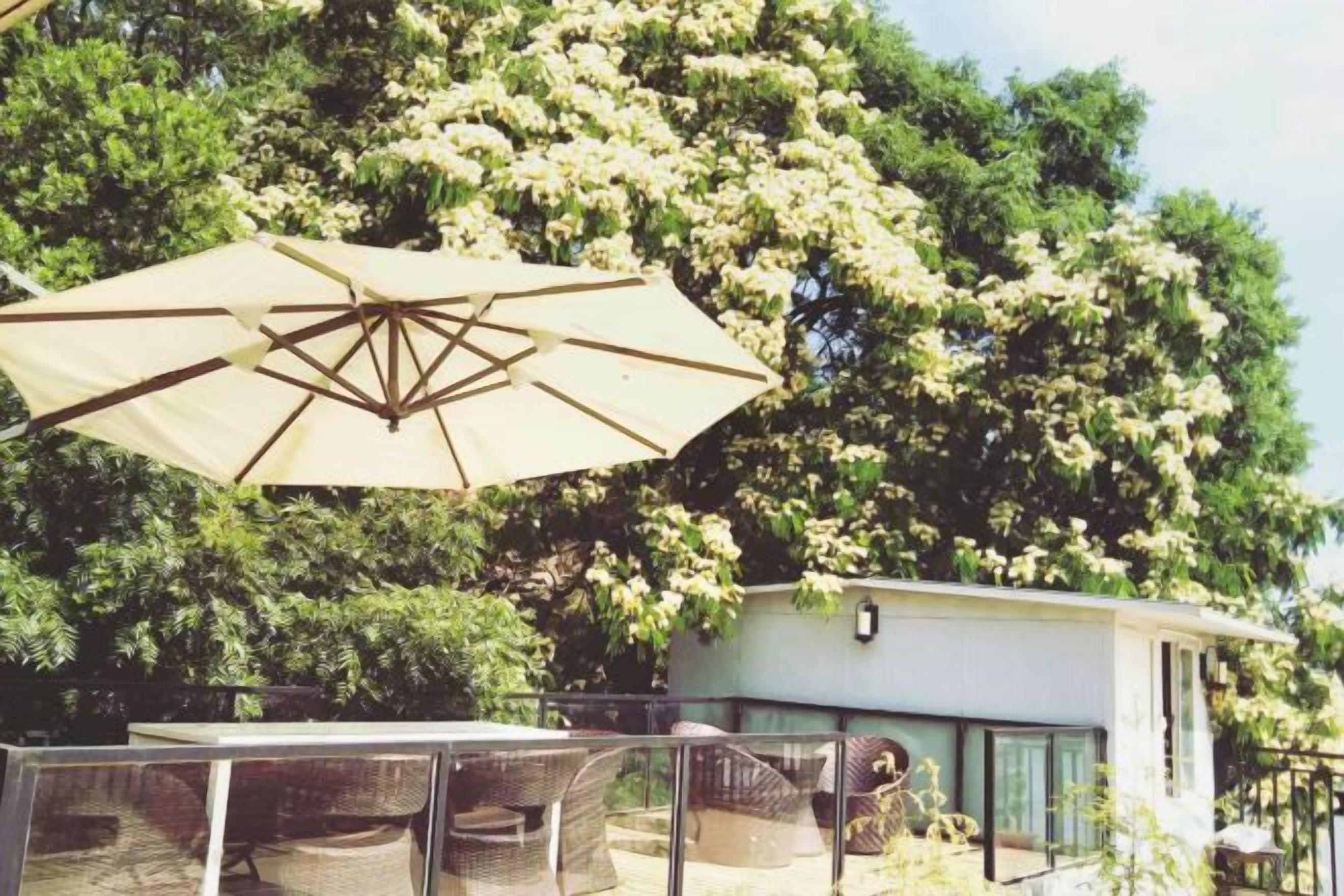 Un área de estar al aire libre con una mesa, sillas, un paraguas grande y un edificio con fachada de vidrio.