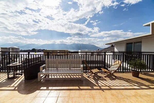 A rooftop terrace with a wooden deck, metal railing, and seating area.