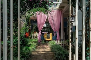 A pathway leading to a building entrance with a wooden deck, surrounded by greenery and a white picket fence.