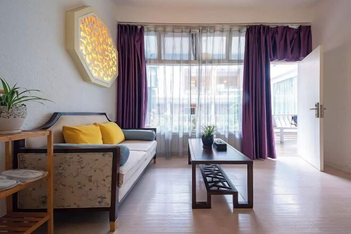 Una sala de estar con sofá, una mesa de centro, una mesita auxiliar, una planta en maceta y una ventana con cortinas.