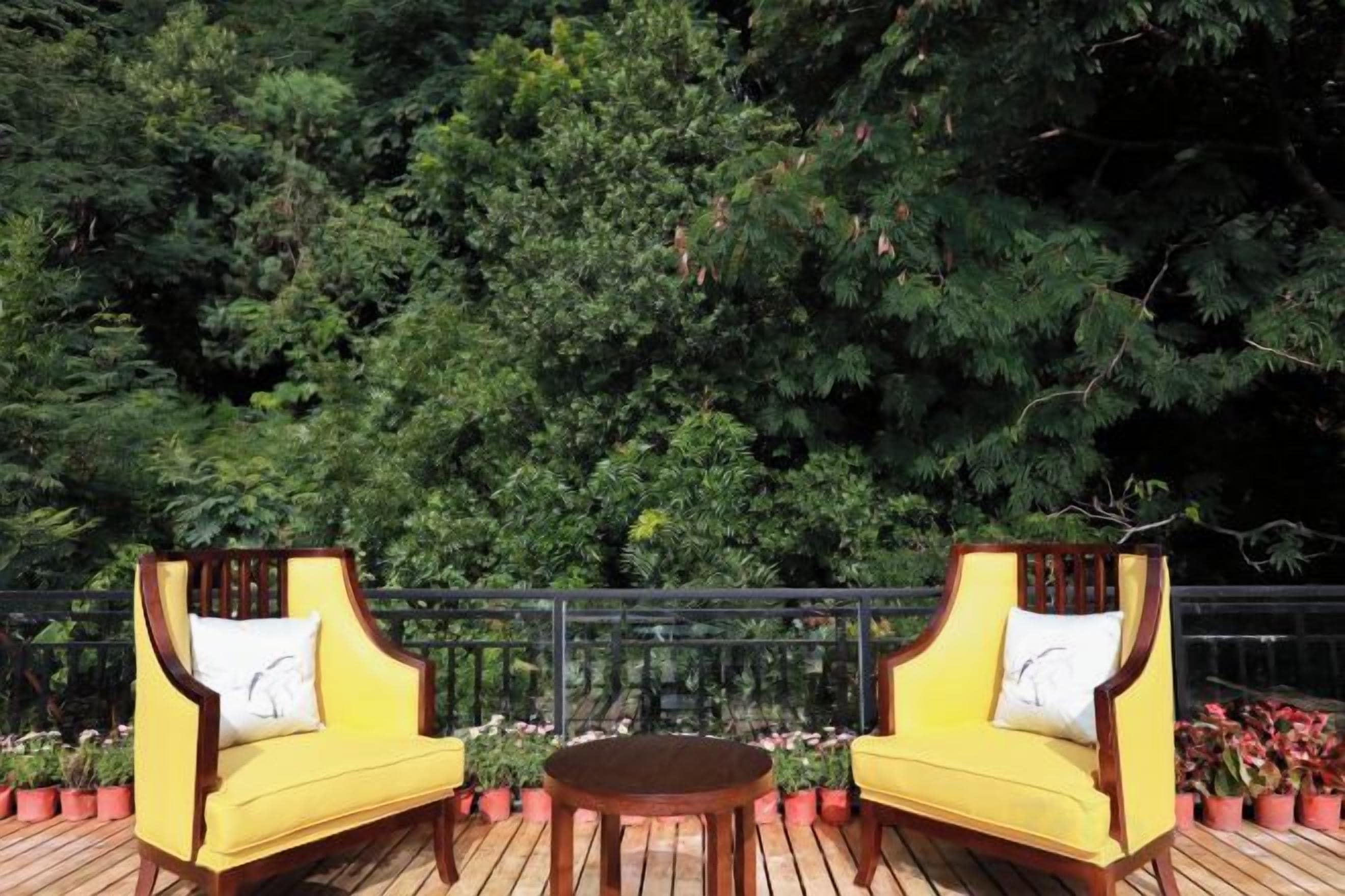 A wooden deck with two yellow chairs and a round table, surrounded by potted plants.
