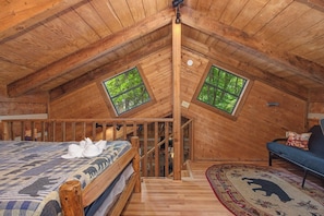 Ein Schlafzimmer im Dachgeschoss mit Holzboden, einem Bett, einer Schlafcouch und zwei Fenstern mit Blick ins Grüne.
