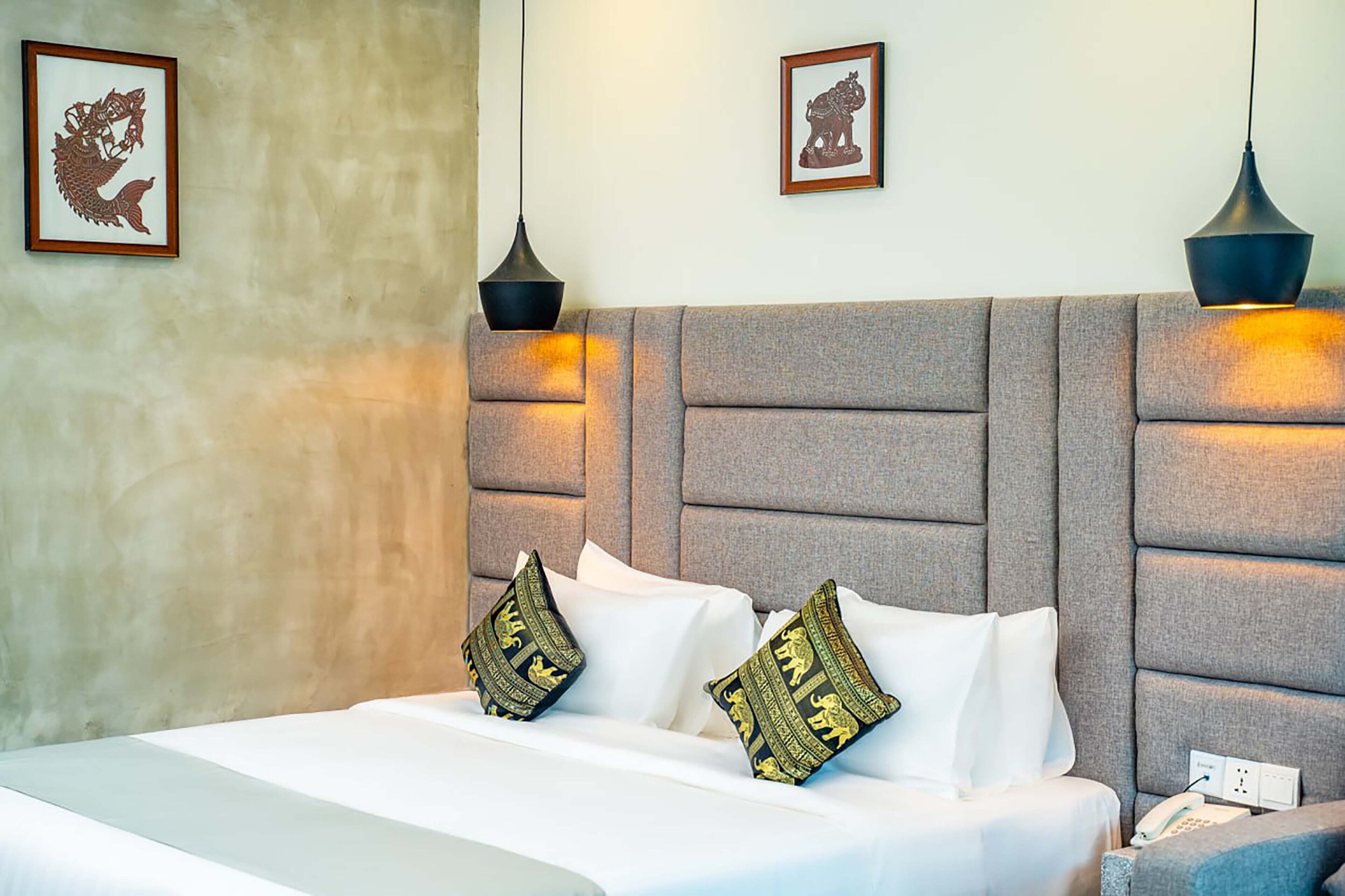 A hotel room with a large bed, two wall-mounted lamps, and two framed pictures on the wall.