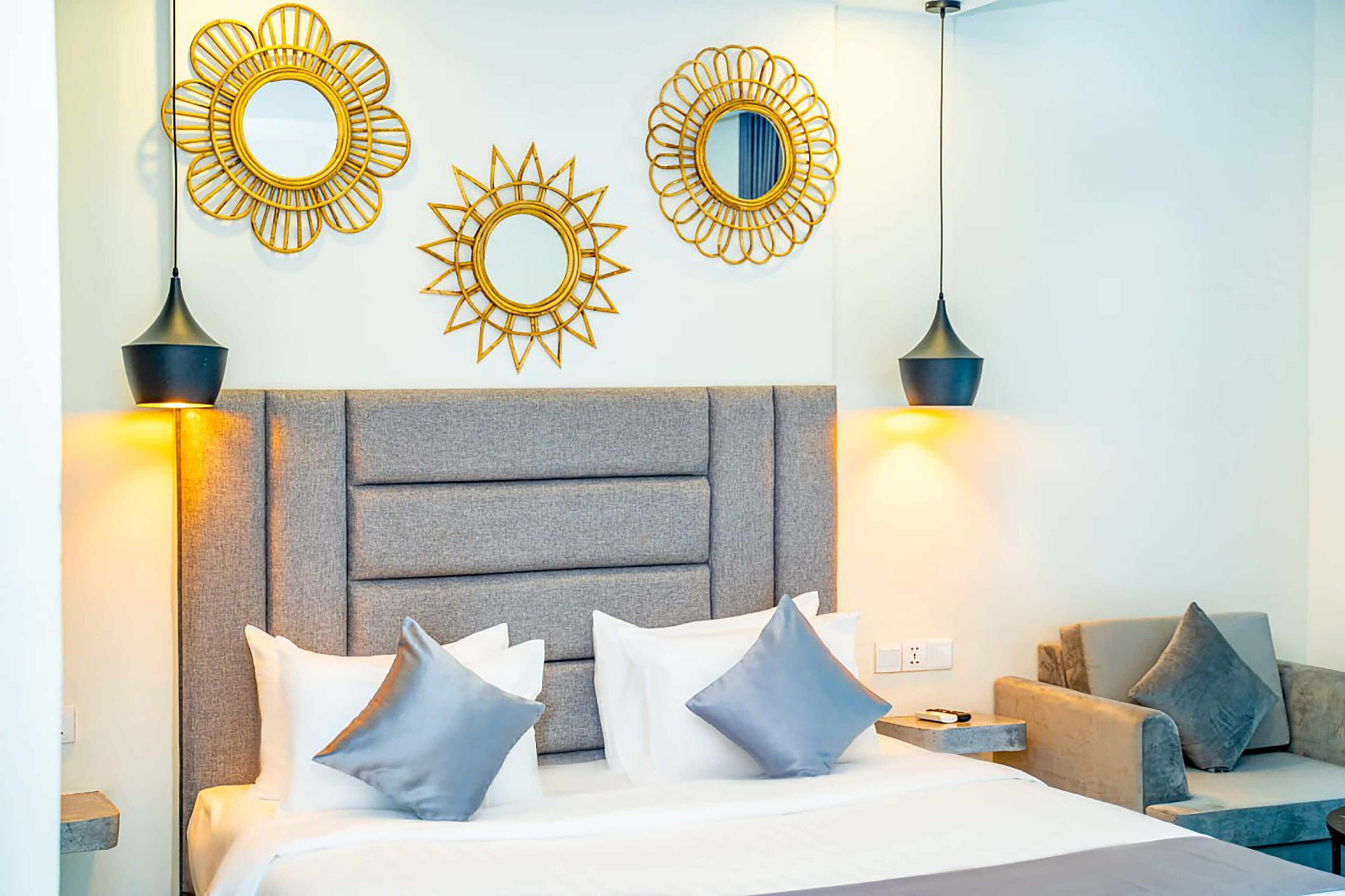 A hotel room with a bed, two wall-mounted mirrors, and two pendant lights.